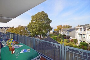 Un balcon avec une table dressée pour le dîner, donnant sur un quartier résidentiel avec des maisons et un grand arbre.