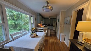 Un comedor con una mesa preparada para dos, una cocina al fondo y vista a zonas verdes exteriores.