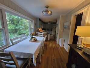 Espaço de refeições com mesa posta para dois, cozinha ao fundo e vista para o verde lá fora.