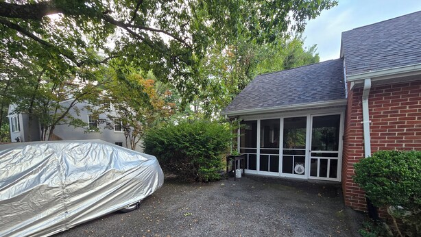 Un automóvil cubierto estacionado en una entrada con una casa y un porche cubierto al fondo.