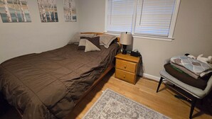 Un dormitorio con cama, mesita de noche, lámpara, silla y ventana con persianas.