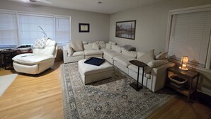 Una sala de estar con un sofá modular, un sillón blanco, una mesita, una lámpara de pie y una alfombra.