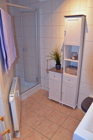 Un bagno con doccia, termosifone, mobile contenitore e una pianta in vaso.