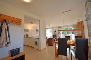 Eine moderne Küche mit Waschmaschine, ein Essbereich mit Stühlen und Tisch sowie ein Wohnbereich mit Sofa.