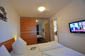 Una habitación de hotel con cama, televisor, armario de madera y espejo.