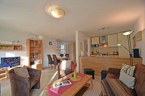 Ein modernes Wohnzimmer mit Fernseher, Sofa, Esstisch und Küchenzeile.