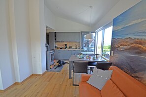 Eine moderne Küche mit grauen Schränken, ein Essbereich mit Tisch und Stühlen sowie ein großes Fenster mit Blick ins Freie.