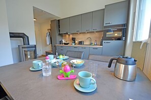 Una cucina moderna con mobili grigi, una caffettiera in acciaio inossidabile e un tavolo da pranzo apparecchiato con tazze, ciotole e un estrattore di frutta.