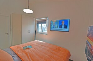 Una camera da letto con un letto, una televisione che mostra un telegiornale, una finestra e una porta.