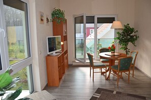Una habitación con una mesa de comedor, sillas, televisión y puerta corredera de vidrio que da a un área exterior.