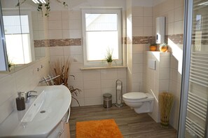 Un baño moderno con un lavamanos blanco grande, un inodoro y una ventana con plantas.