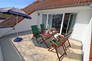 A patio with a table set for four, surrounded by green chairs, and a blue umbrella providing shade. - Just 250 meters from the sandy Baltic Sea beach, balcony with patio furniture and a beach umbrella (Glowe)