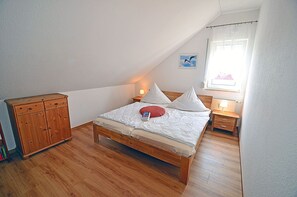 A bedroom with a wooden bed, a nightstand, a dresser, and a window with a curtain. - Just 250 meters from the sandy Baltic Sea beach, balcony with patio furniture and a beach umbrella (Glowe)