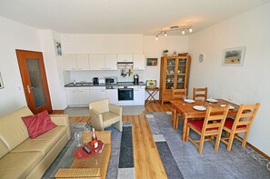 A compact living space with a kitchenette, a dining area, and a seating area with a sofa and chairs. - Just 250 meters from the sandy Baltic Sea beach, balcony with patio furniture and a beach umbrella (Glowe)
