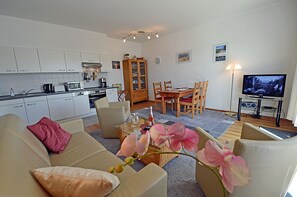 A living room with a sofa, a coffee table, and a TV stand with a television. - Just 250 meters from the sandy Baltic Sea beach, balcony with patio furniture and a beach umbrella (Glowe)