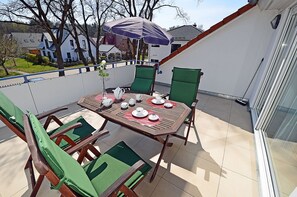 A balcony with a table set for tea, chairs, and a purple umbrella. - Just 250 meters from the sandy Baltic Sea beach, balcony with patio furniture and a beach umbrella (Glowe)