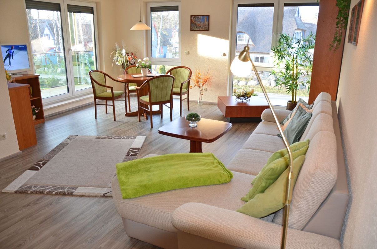 Een woonkamer met een bank, een eettafel met stoelen, een televisie en een raam met uitzicht op een huis.