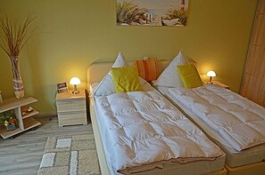 A bedroom with two single beds, a bedside table with a lamp, a small shelf with decorative items, and a painting on the wall. - Just 800 meters from the sandy Baltic Sea beach, Wi-Fi available, balcony with patio furniture (Glowe)