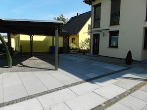 A covered outdoor area with a paved walkway leading to a yellow building with a black roof. - Just 800 meters from the sandy Baltic Sea beach, Wi-Fi available, balcony with patio furniture (Glowe)