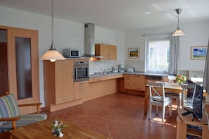 A compact kitchen with wooden cabinets, a microwave, an oven, and a dining area with a table and chairs. - Only 500 meters from the sandy Baltic Sea beach, patio with patio furniture, Internet available (Glowe)