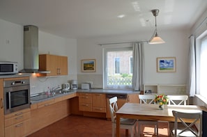 A compact kitchen with modern appliances, a dining area with a wooden table and chairs, and a window with a view of a brick building. - Only 500 meters from the sandy Baltic Sea beach, patio with patio furniture, Internet available (Glowe)