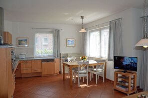 A compact kitchen with a dining area, a television, and a window with curtains. - Only 500 meters from the sandy Baltic Sea beach, patio with patio furniture, Internet available (Glowe)