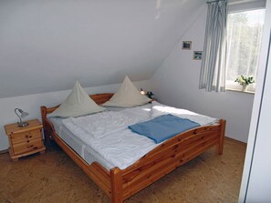 A bedroom with a wooden bed, a nightstand, a window with curtains, and a small plant on the windowsill. - Only 500 meters from the sandy Baltic Sea beach, balcony with patio furniture, internet available (Glowe)