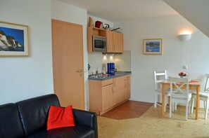 A compact living space with a kitchenette, a dining area, and a sofa with a red pillow. - Only 500 meters from the sandy Baltic Sea beach, balcony with patio furniture, Internet available (Glowe)