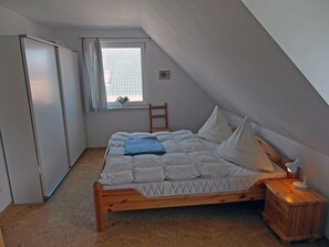 Un dormitorio con una cama de madera, una mesita de noche, una ventana con cortinas y un armario.