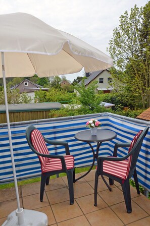 An outdoor seating area with a table and chairs, a white umbrella, and a blue-striped wall. - Only 500 meters from the sandy Baltic Sea beach, balcony with patio furniture, Internet available (Glowe)