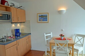 A kitchen with wooden cabinets, a microwave, and a coffee maker. There is a dining table with white chairs and a vase of flowers. - Only 500 meters from the sandy Baltic Sea beach, balcony with patio furniture, Internet available (Glowe)