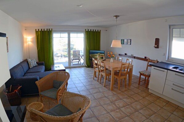 Un espacio habitable pequeño con sofá, sillas de mimbre, una mesa de comedor y una kitchenette.