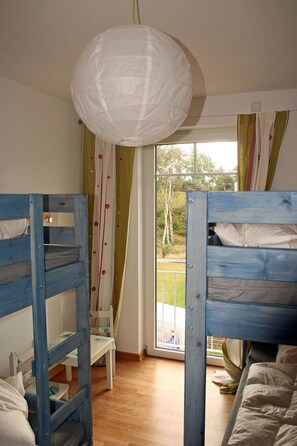 Una habitación con literas, una lámpara colgante, una ventana con cortinas y vistas al exterior.