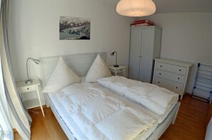 A bedroom with a bed, bedside tables, a wardrobe, and a hanging light fixture. - 2nd floor, ocean view, high-end amenities, 25 m from the sandy beach (Baltic Sea) (Juliusruh)