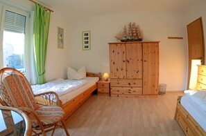 Quarto com cama de madeira, guarda-roupa de madeira, uma cadeira, mesa de cabeceira com abajur e um modelo de navio em cima do guarda-roupa.