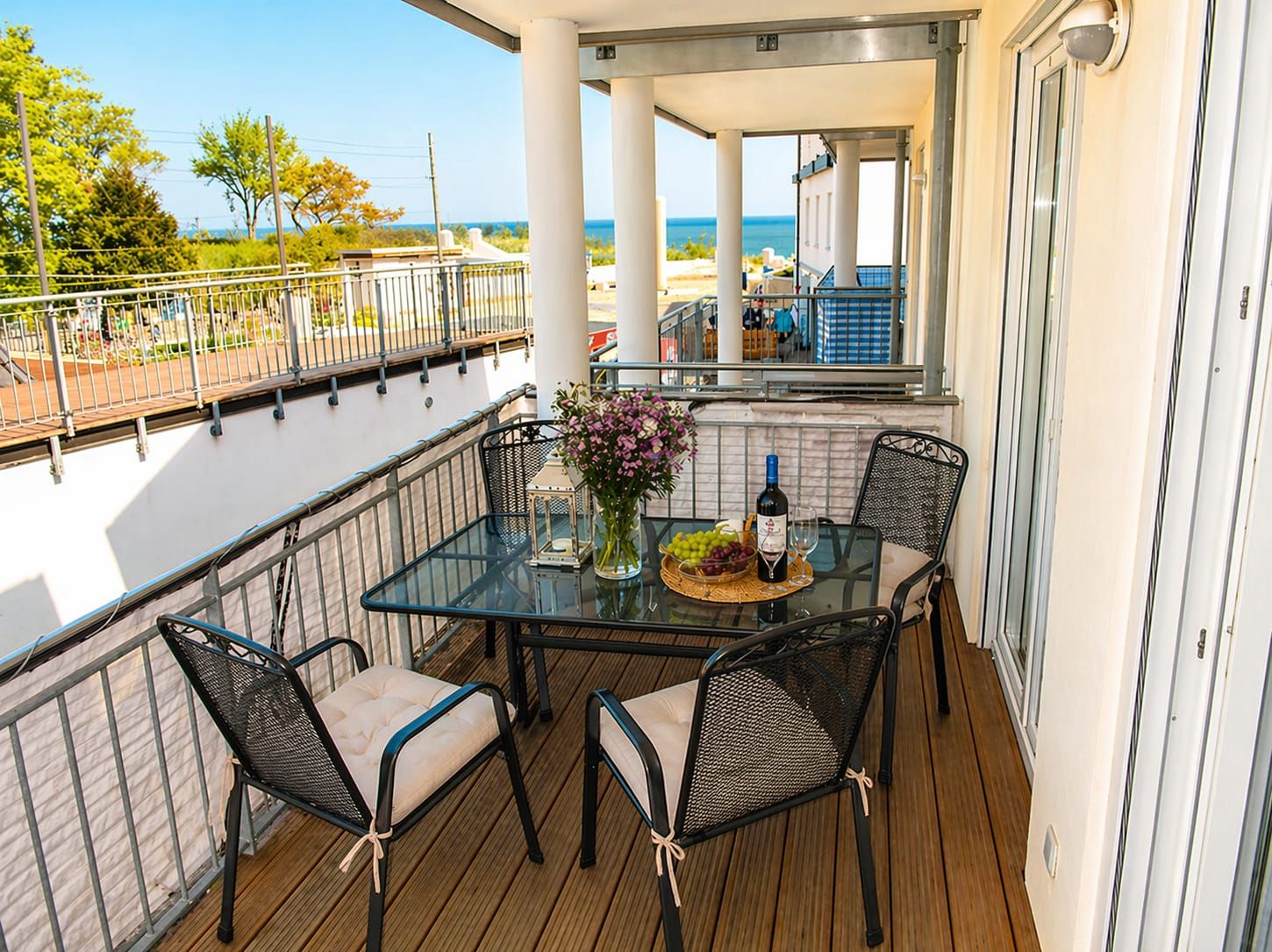 Ein Balkon mit Glastisch, vier Stühlen, einer Weinflasche und einem Blumenstrauß.