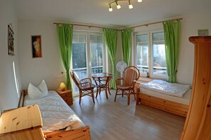 Quarto com uma cama, duas cadeiras, uma mesinha e uma janela com cortinas.