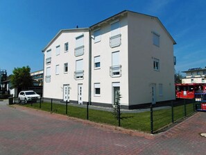 Ein mehrgeschossiges Wohngebäude mit flacher Fassade, Balkonen und einem gepflasterten Auffahrt.