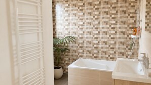 Ein modernes Badezimmer mit einer weißen Badewanne, einem hölzernen Waschtisch, einem gefliesten Boden und einer Topfpflanze.