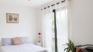Ein Schlafzimmer mit Bett, Nachttisch, Lampe und Blick ins Freie durch ein Fenster.