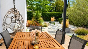 Ein Holztisch mit Stühlen im Freien, ein Hängesessel und eine Glasvase mit Blumen.