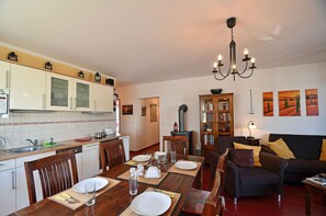 A dining area with a wooden table set for four, a kitchen with white cabinets, and a living room with a black sofa and a fireplace. - Apartment in a central location in Juliusruh, 25 m from the sandy beach with a view of the sea (Juliusruh)