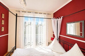 A bedroom with a bed, a window with curtains, a bedside table with a lamp, and a mirror on the wall. - Apartment in a central location in Juliusruh, 25 m from the sandy beach with a view of the sea (Juliusruh)