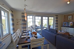 A dining area with a table set for four, a sofa, and a television in the background. - 2nd floor with ocean view, upscale amenities, 25 m from the sandy beach (Baltic Sea) (Juliusruh)