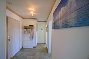 A hallway with a tiled floor, a coat rack with bags, a door, and a painting of a seascape. - 2nd floor with ocean view, upscale amenities, 25 m from the sandy beach (Baltic Sea) (Juliusruh)