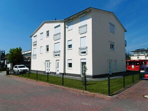 A multi-story residential building with a flat facade, a fenced yard, and a parked car. - 2nd floor with ocean view, upscale amenities, 25 m from the sandy beach (Baltic Sea) (Juliusruh)