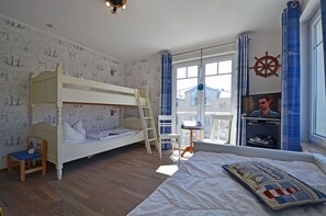 A room with a bunk bed, a desk with a chair, a television, and a large window with curtains. - 2nd floor with ocean view, upscale amenities, 25 m from the sandy beach (Baltic Sea) (Juliusruh)