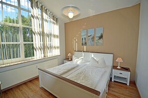 A bedroom with a large window, a bed, bedside tables, and a wall-mounted light fixture. - 2nd floor with ocean view, high-end amenities, just 30 m from the sandy beach (Baltic Sea) (Juliusruh)