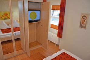 Quarto com cama, televisão, guarda-roupa e janela com cortinas.