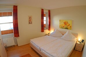 Ein Doppelbett mit Kopfteil, Nachttische, ein Gemälde und ein Fenster mit Vorhängen.